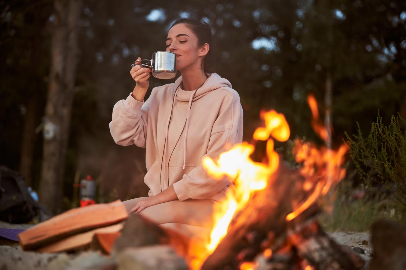 Young woman sipping coffee by a campfire in a North Dakota Campground